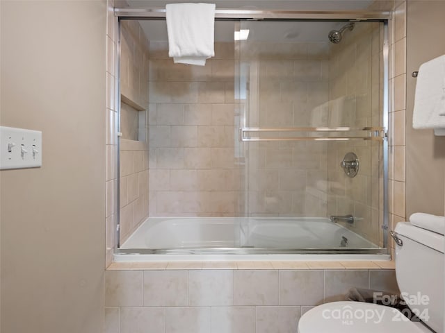 bathroom with toilet and bath / shower combo with glass door