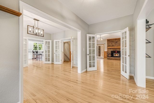 interior space featuring french doors, light hardwood / wood-style flooring, a chandelier, and a brick fireplace