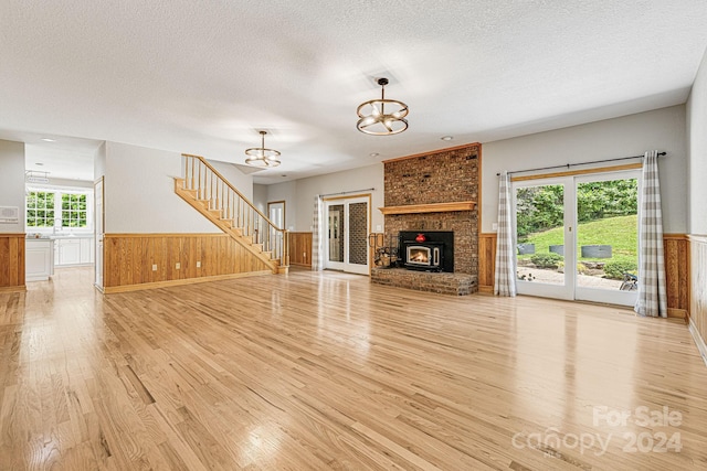 unfurnished living room featuring a textured ceiling, light hardwood / wood-style floors, a notable chandelier, and wood walls