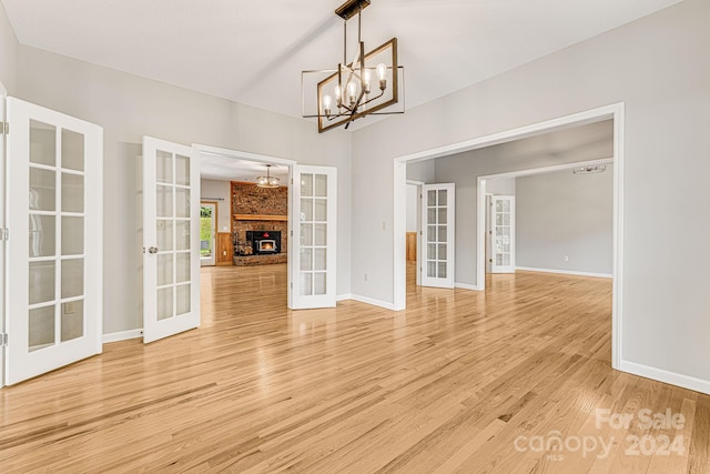 unfurnished dining area with a brick fireplace, french doors, a chandelier, and wood-type flooring