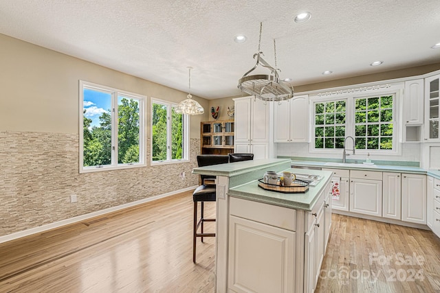 kitchen with pendant lighting, white cabinets, sink, a kitchen island, and a kitchen bar