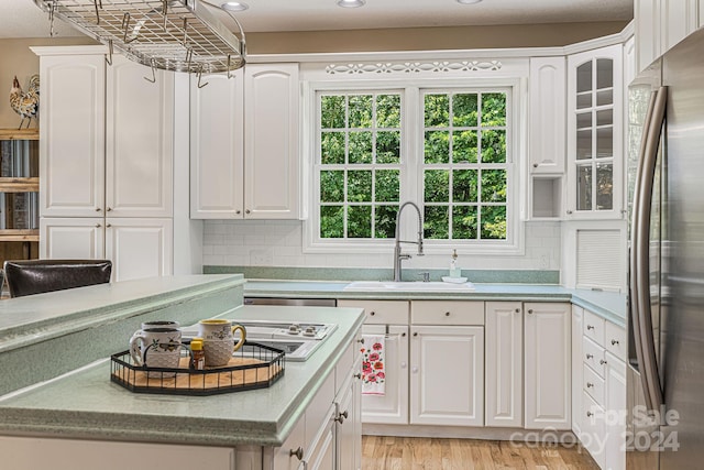 kitchen featuring sink, stainless steel fridge, light hardwood / wood-style floors, decorative backsplash, and white cabinets