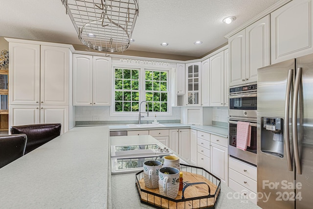 kitchen featuring white cabinetry, sink, tasteful backsplash, a textured ceiling, and appliances with stainless steel finishes