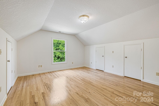 additional living space featuring light hardwood / wood-style floors, a textured ceiling, and vaulted ceiling