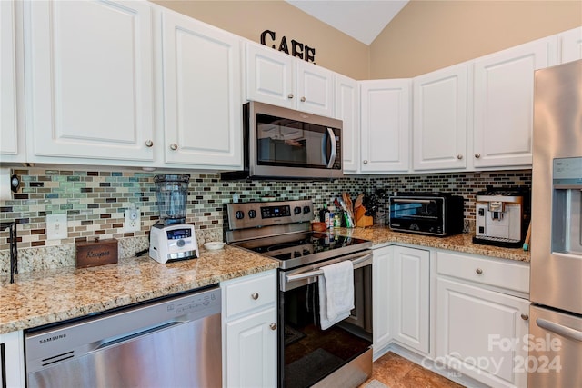 kitchen with lofted ceiling, backsplash, light stone countertops, appliances with stainless steel finishes, and white cabinetry