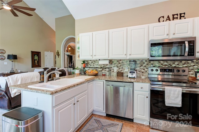 kitchen with kitchen peninsula, light stone countertops, stainless steel appliances, sink, and white cabinets