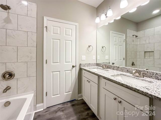 bathroom featuring wood-type flooring, tiled shower / bath combo, vanity with extensive cabinet space, and double sink