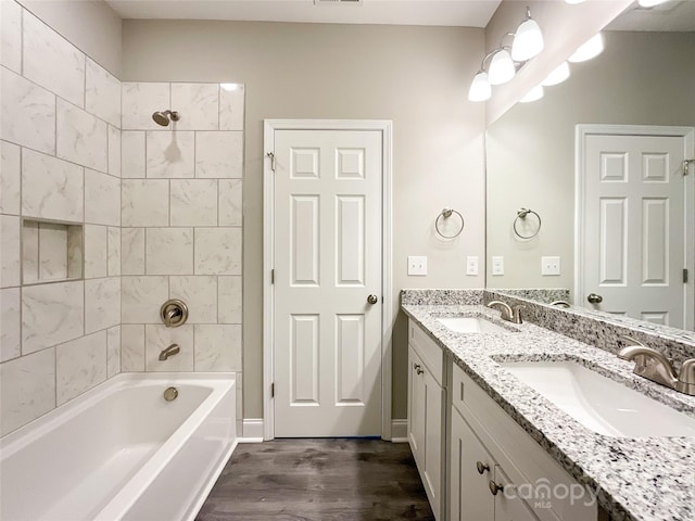 bathroom featuring tiled shower / bath, vanity with extensive cabinet space, hardwood / wood-style flooring, and double sink