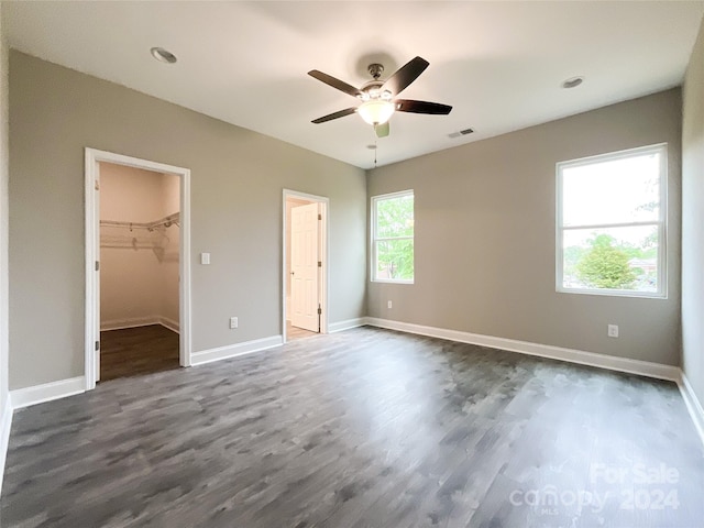 unfurnished bedroom with ceiling fan, dark hardwood / wood-style flooring, a walk in closet, and multiple windows