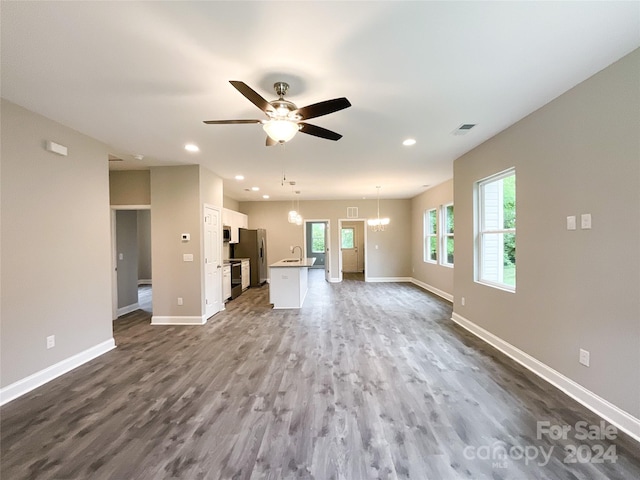 unfurnished living room with ceiling fan with notable chandelier, sink, and hardwood / wood-style floors