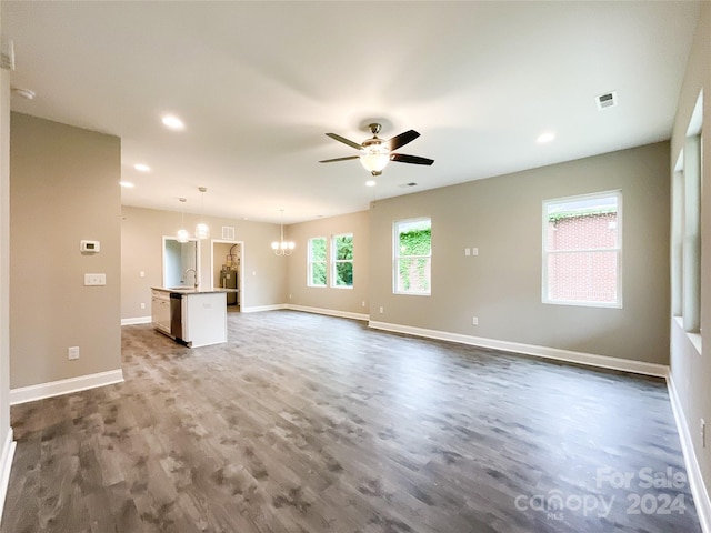 unfurnished living room featuring wood-type flooring and ceiling fan with notable chandelier