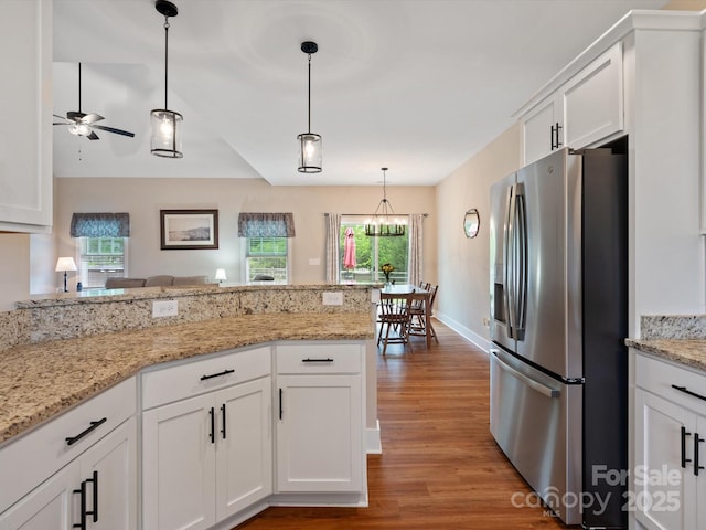 kitchen featuring white cabinetry, pendant lighting, stainless steel fridge, and light stone counters