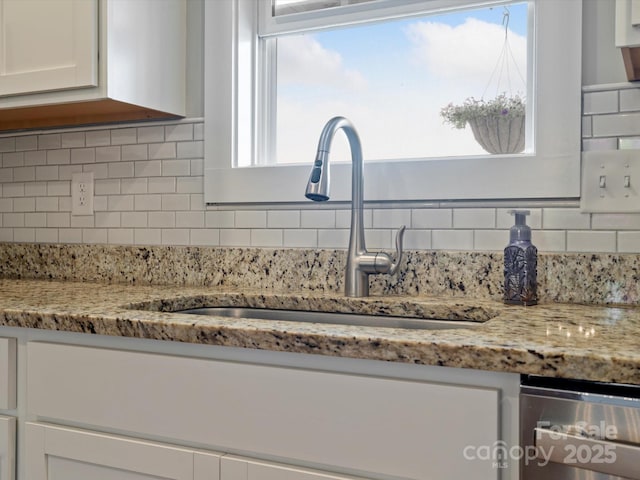 interior details featuring white cabinetry, sink, light stone counters, and backsplash