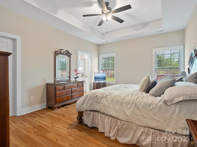 bedroom with ceiling fan, a raised ceiling, and light hardwood / wood-style flooring