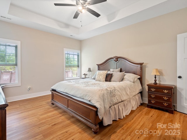 bedroom with multiple windows, a tray ceiling, light hardwood / wood-style floors, and ceiling fan