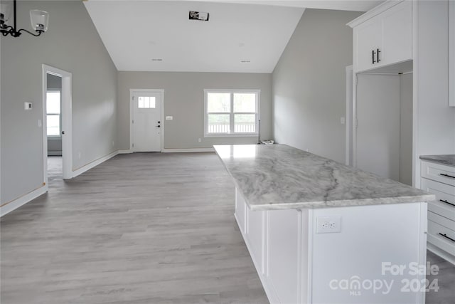 kitchen with white cabinetry, high vaulted ceiling, a kitchen island, light stone countertops, and light hardwood / wood-style floors