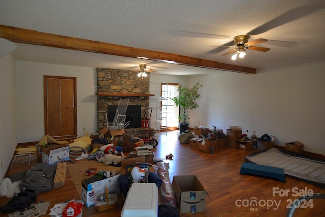 living room with a fireplace, dark hardwood / wood-style flooring, beam ceiling, ceiling fan, and a textured ceiling