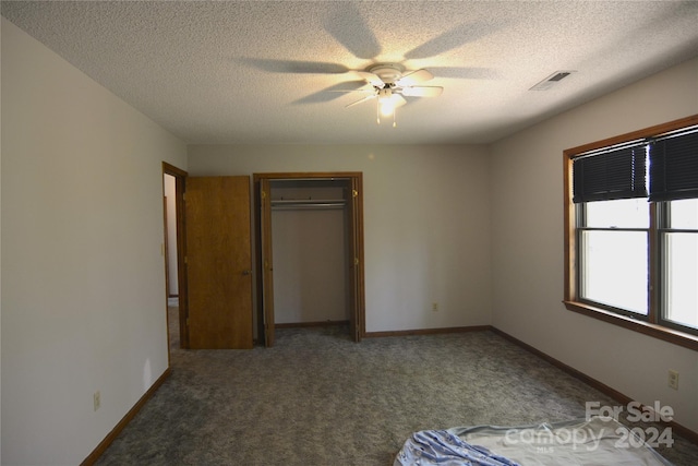 unfurnished bedroom with a closet, ceiling fan, dark carpet, and a textured ceiling