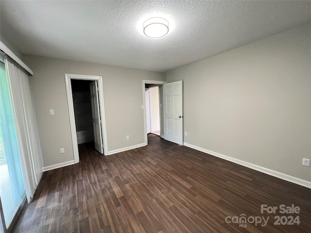 unfurnished bedroom featuring a closet, a textured ceiling, dark wood-type flooring, and a walk in closet