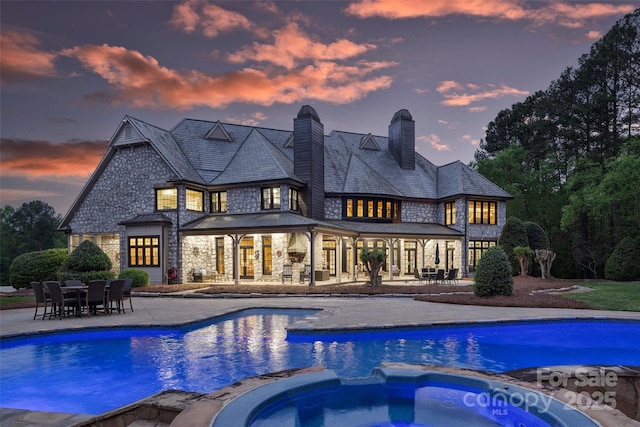 back house at dusk featuring a swimming pool with hot tub and a patio area