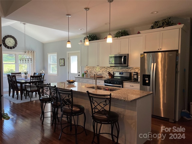 kitchen with stainless steel appliances, white cabinets, vaulted ceiling, and light stone counters