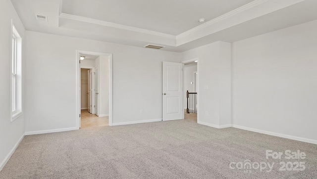 empty room featuring crown molding, a tray ceiling, and light colored carpet