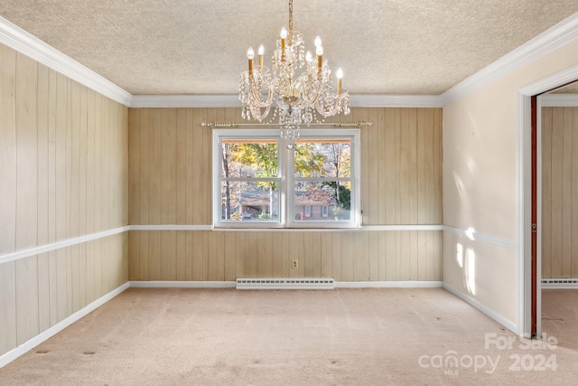 empty room featuring crown molding, wooden walls, baseboard heating, carpet floors, and a chandelier