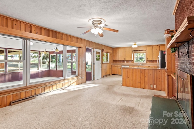 kitchen featuring stainless steel refrigerator, sink, wood walls, light colored carpet, and a textured ceiling