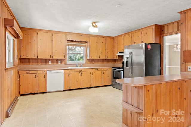 kitchen with wood walls, sink, stainless steel appliances, and an inviting chandelier