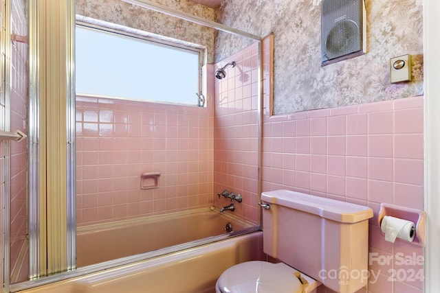 bathroom featuring toilet, combined bath / shower with glass door, and tile walls