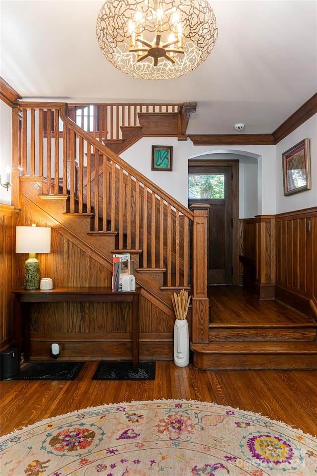 stairway featuring hardwood / wood-style floors, wood walls, ornamental molding, and an inviting chandelier