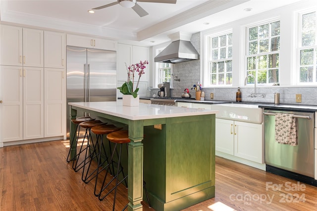 kitchen with hardwood / wood-style floors, a center island, white cabinets, wall chimney range hood, and appliances with stainless steel finishes