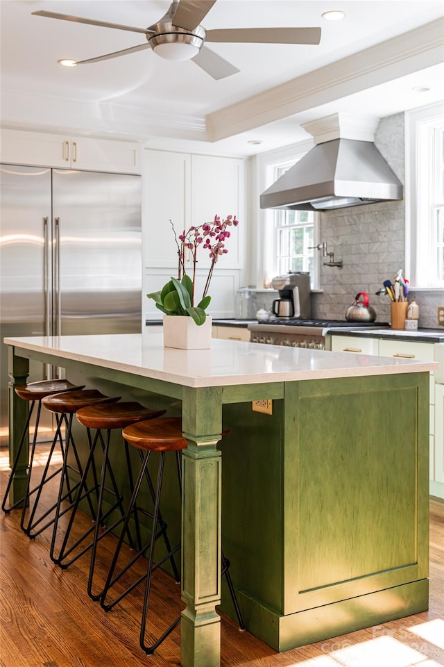 kitchen featuring high end refrigerator, a center island, wall chimney range hood, and light hardwood / wood-style flooring