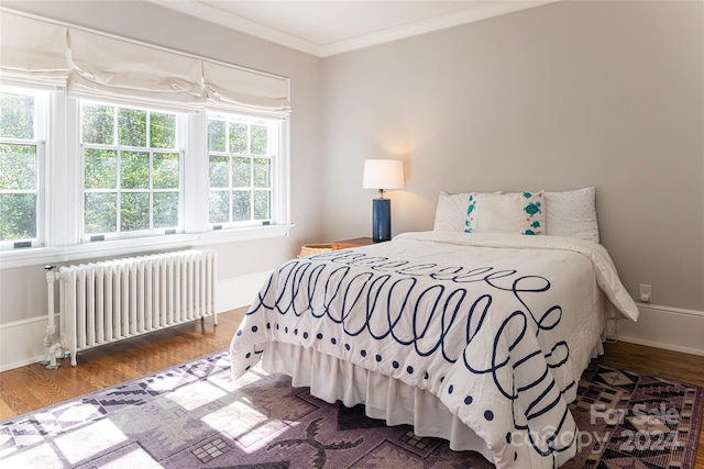 bedroom featuring hardwood / wood-style floors, radiator heating unit, and ornamental molding