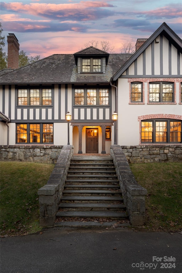 back house at dusk with a lawn and a balcony