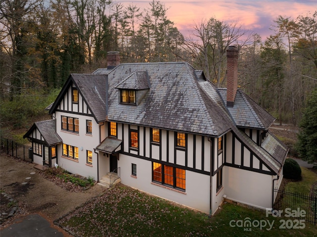 30 Cedarcliff Rd, Asheville, NC 28803 - back of house at dusk featuring a chimney, stucco siding, view of scattered trees, and a high end roof