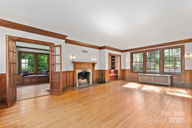 30 Cedarcliff Rd, Asheville, NC 28803 - unfurnished living room featuring radiator heating unit, wainscoting, light wood finished floors, a fireplace with flush hearth, and crown molding