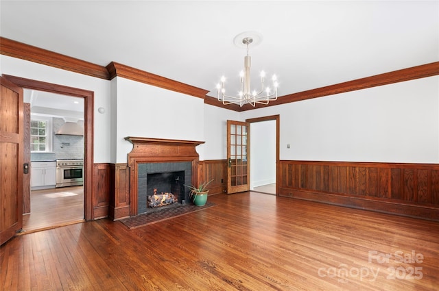 30 Cedarcliff Rd, Asheville, NC 28803 - unfurnished living room featuring hardwood / wood-style flooring, a chandelier, a warm lit fireplace, a wainscoted wall, and ornamental molding