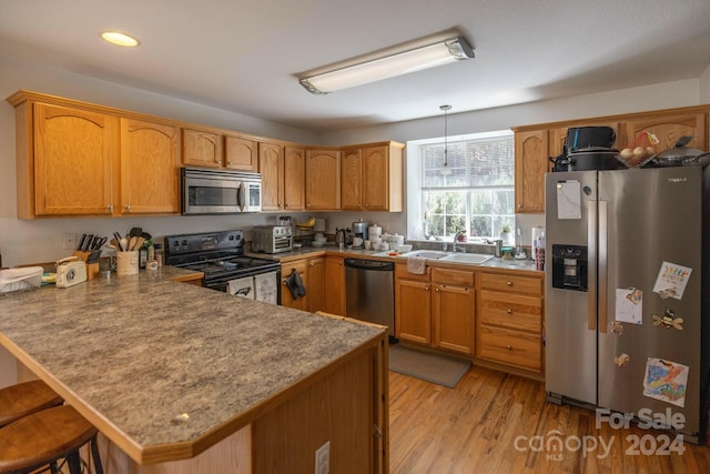 kitchen with kitchen peninsula, a kitchen bar, appliances with stainless steel finishes, light hardwood / wood-style flooring, and pendant lighting