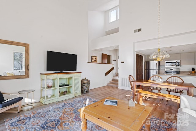 living room with a towering ceiling, a notable chandelier, and light hardwood / wood-style flooring