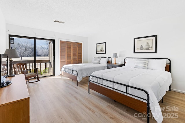 bedroom with a textured ceiling, access to exterior, and light wood-type flooring