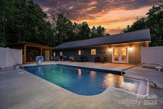 pool at dusk with french doors and a patio area