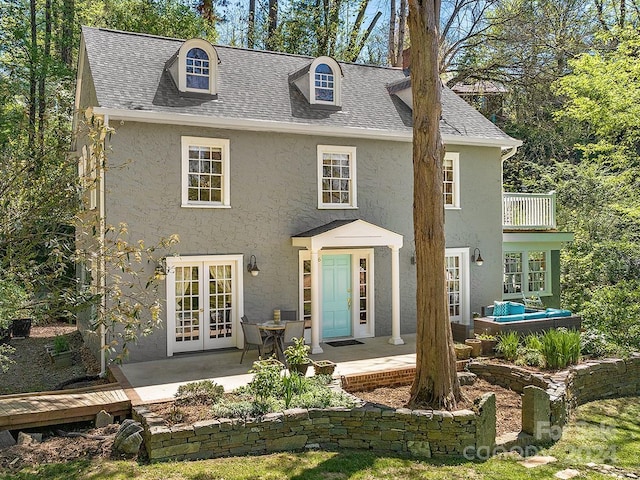 view of front facade with french doors, a patio, stucco siding, a shingled roof, and a balcony