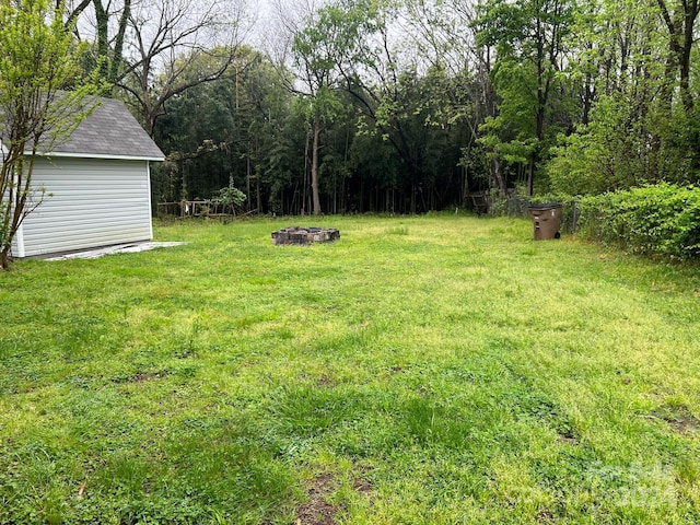 view of yard with an outbuilding, a wooded view, and an outdoor fire pit