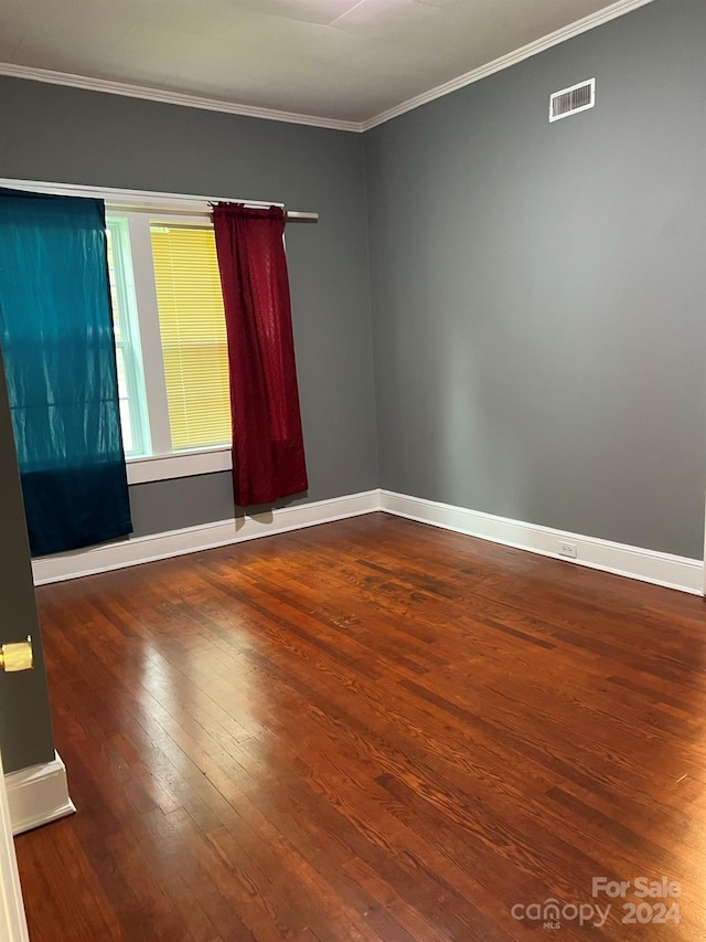 empty room featuring visible vents, ornamental molding, baseboards, and wood finished floors