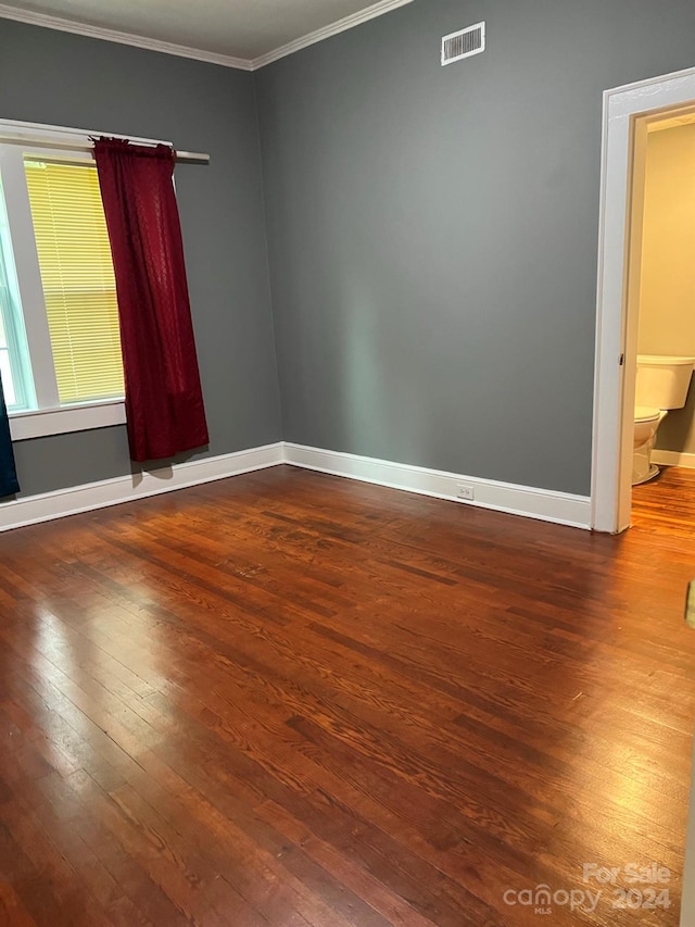 empty room with dark wood-type flooring, baseboards, visible vents, and ornamental molding