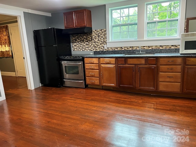 kitchen with a sink, under cabinet range hood, stainless steel electric stove, freestanding refrigerator, and white microwave