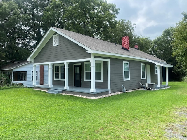 back of property featuring a lawn, central AC, covered porch, roof with shingles, and a chimney