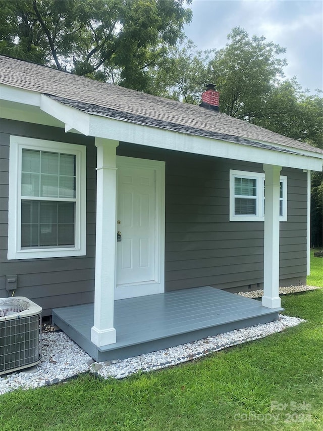 doorway to property featuring roof with shingles, central AC unit, a chimney, and a lawn