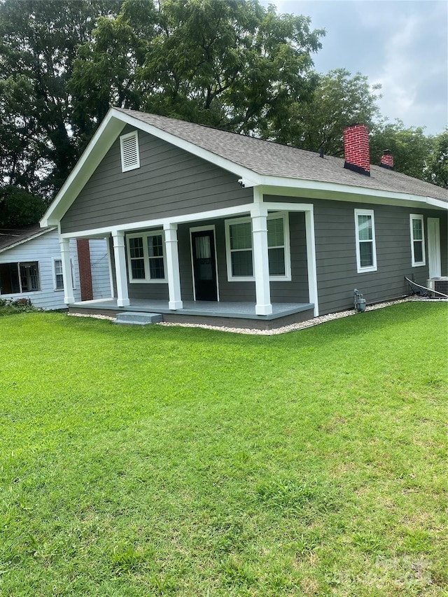 back of property featuring a porch, a lawn, roof with shingles, and a chimney